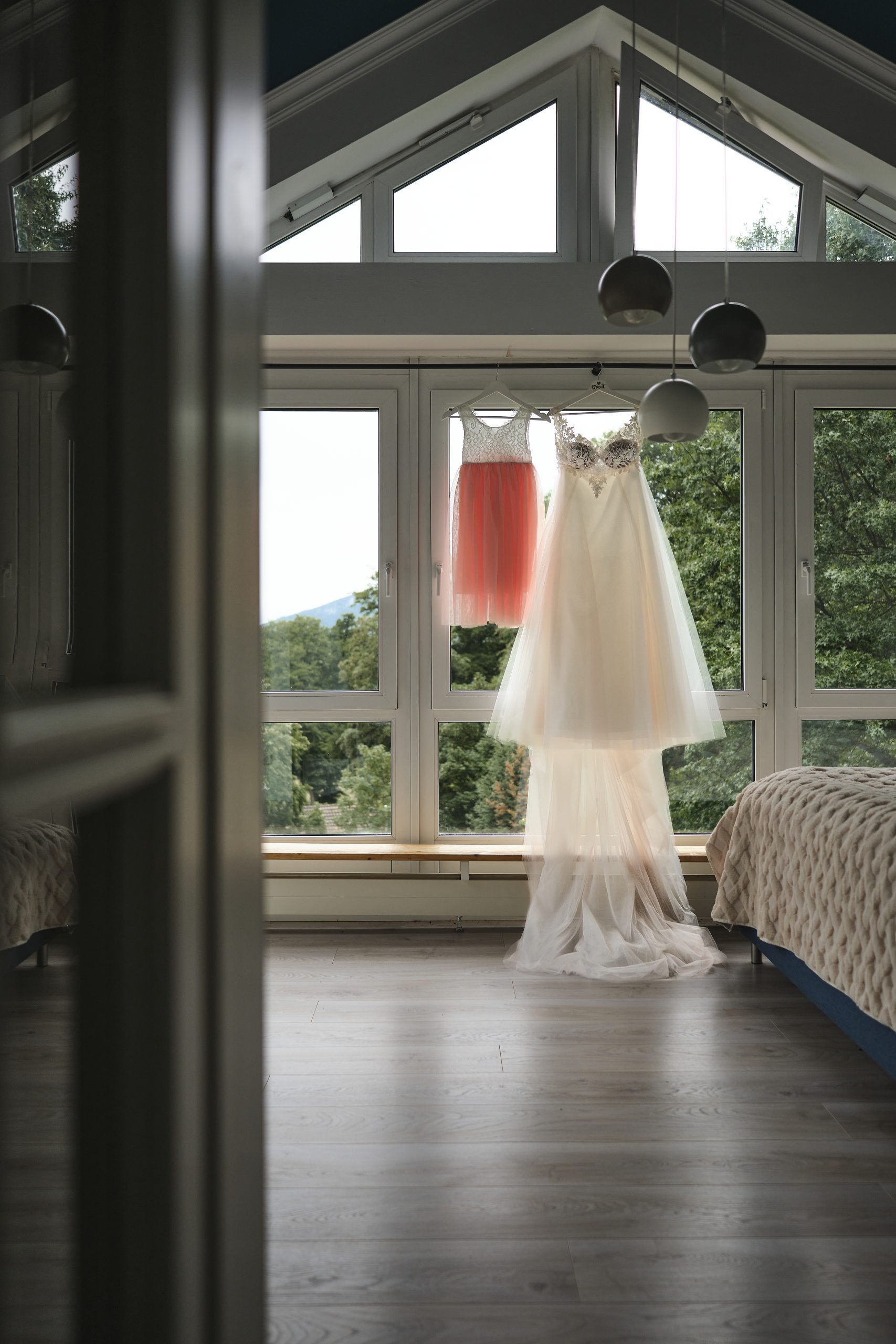 Das Brautkleid und das Kleid der kleinen Tochter hängen vor Fenster und warten darauf angezogen zu werden.