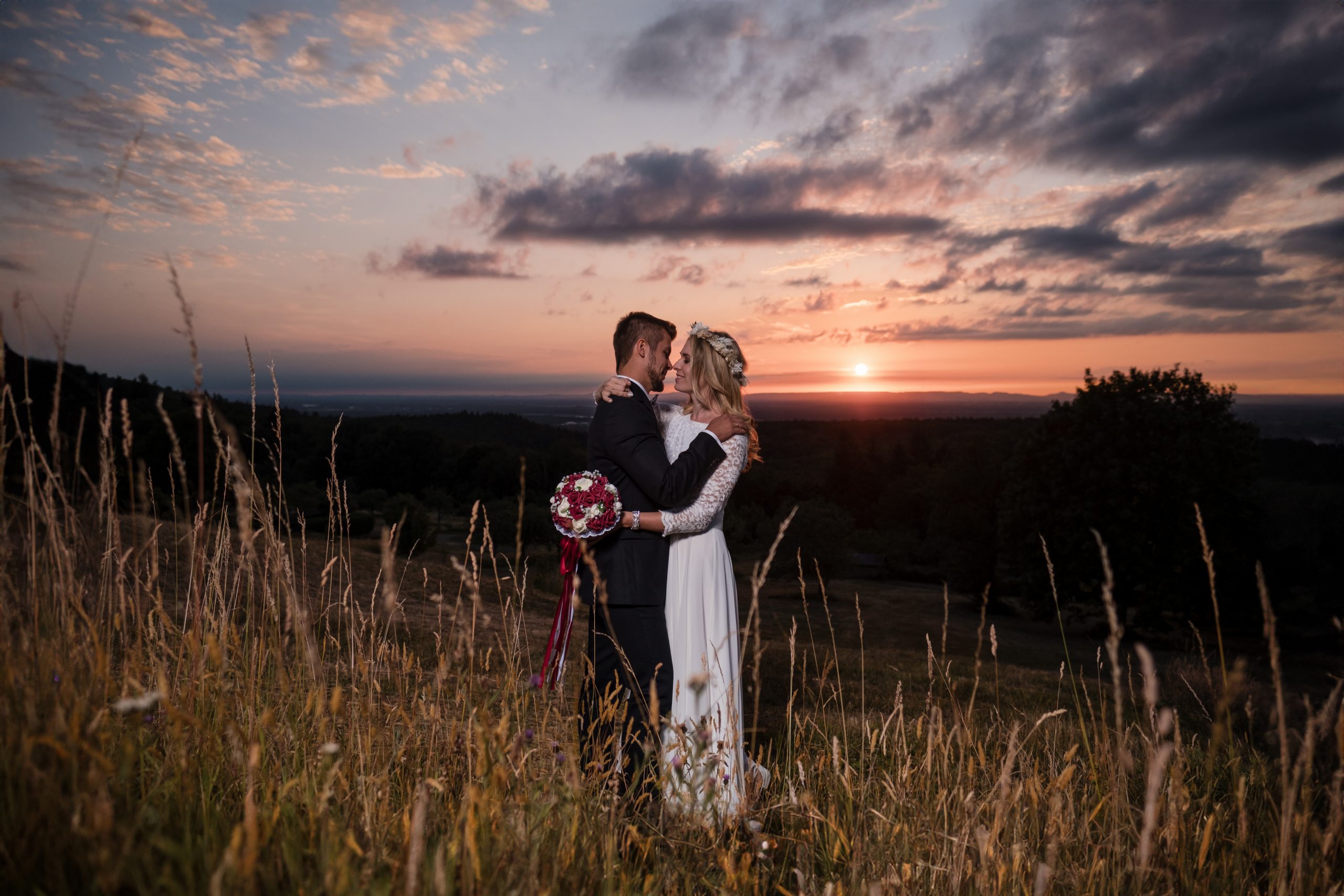 Ein Feld bei Sonnenuntergang ist SChauplatz für eine innige Umarmung eines Paares