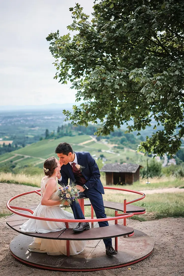 Hochzeitsfoto eines Brautpaares auf einem Karussell bei der Burg Windeck in Bühl mit malerischem Blick ins Rebland