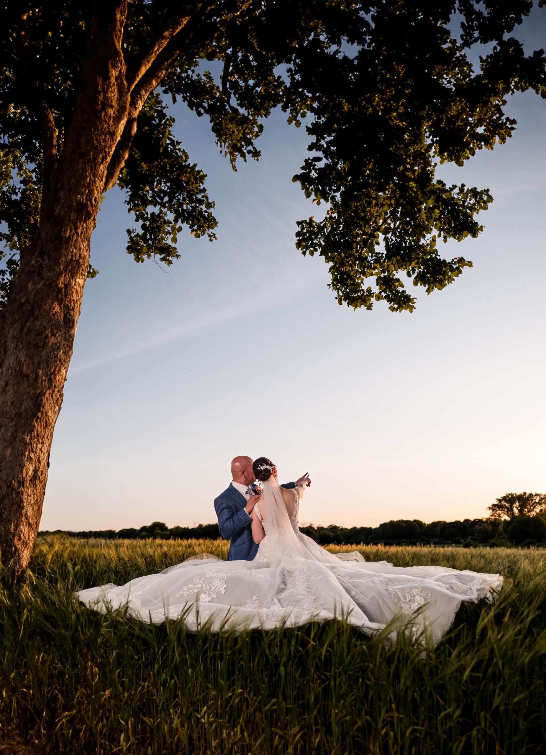 Ein Brautpaar im Kornfeld, eingerahmt von einem Baum zeigt gemeinsam in die Ferne