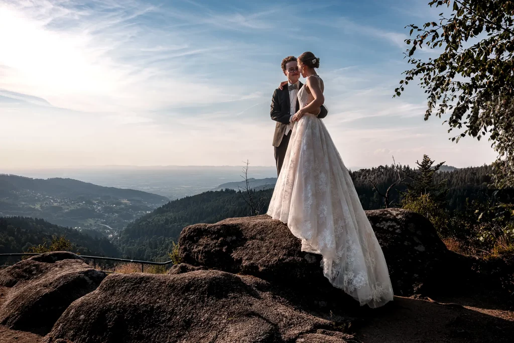 Ein Brautpaar steht auf dem Aussichtspunkt Wiedenfelsen vor athemberaubender Kulisse mit Blick ins Tal von Bühl kurz vor Sonneuntergang, aufegnommen von dem Hochzeitsfotograf bei Bühl Volker Herzing